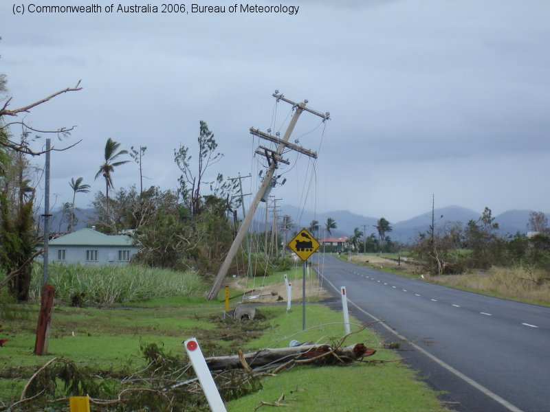 Bureau of Meteorology photograph showing leaning power poles along a rural road near Innisfail with fallen trees and debris on the verge following Cyclone Larry